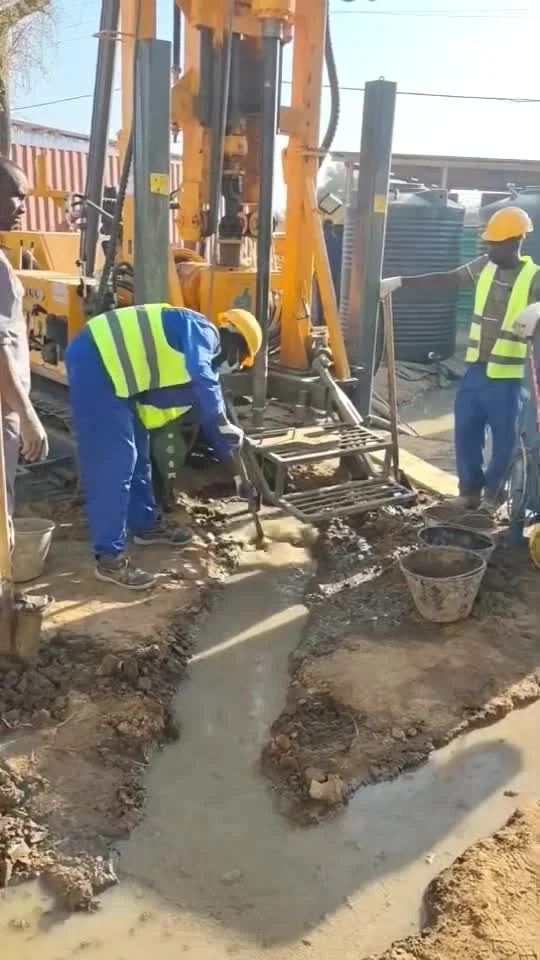 Drilling crew beside a crawler drilling rig and drilling-fluid return channel.